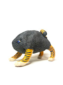 A small sculptural figurine of a four-legged creature with a dark charcoal-black textured body, bright orange and yellow striped legs, and blue eyes, photographed on a plain white studio background.