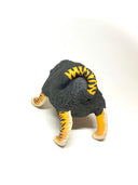 A small sculptural figurine of a four-legged creature with a dark charcoal-black textured body, bright orange and yellow striped legs, and blue eyes, photographed on a plain white studio background.