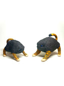 Two small sculptural cat figurines on a plain white studio background. Each cat has a dark charcoal body with bright orange and black tiger-like stripes on the legs, paws, and tail, plus small blue eyes.