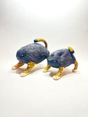Two small sculptural cat figurines on a plain white studio background. Each cat has a dark charcoal body with bright orange and black tiger-like stripes on the legs, paws, and tail, plus small blue eyes.