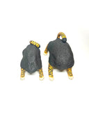 Two small sculptural cat figurines on a plain white studio background. Each cat has a dark charcoal body with bright orange and black tiger-like stripes on the legs, paws, and tail, plus small blue eyes.