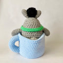 Crochet sculpture of a blue mug with a pink heart. Inside the mug is Totoro with a green scarf. A dust sprite sits atop its head.