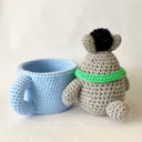 Crochet sculpture of a blue mug with a pink heart. Next to the mug is Totoro with a green scarf. A dust sprite sits atop its head.