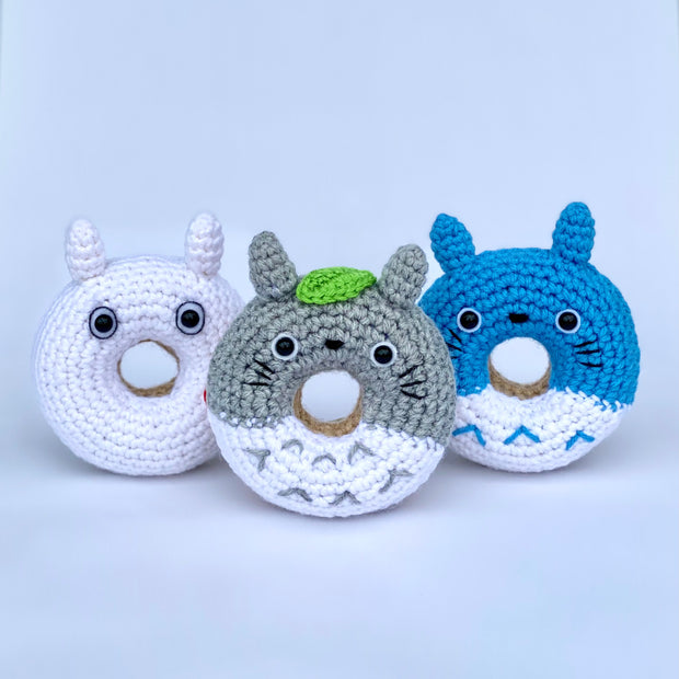 3 crocheted donuts fashioned to look like characters from My Neighbor Totoro. Variants are Totoro with a leaf atop its head, blue Totoro and a simplistic white Totoro.
