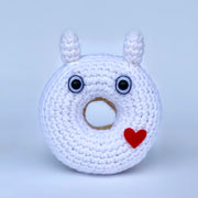 A crocheted donut fashioned to look like a simplistic white Totoro, with wide eyes and a small red heart on its side.