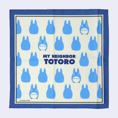 Cream colored handkerchief with a thick blue border featuring a repeating pattern of small, blue chibi Totoros with "My Neighbor Totoro" written in the center in bold blue font.
