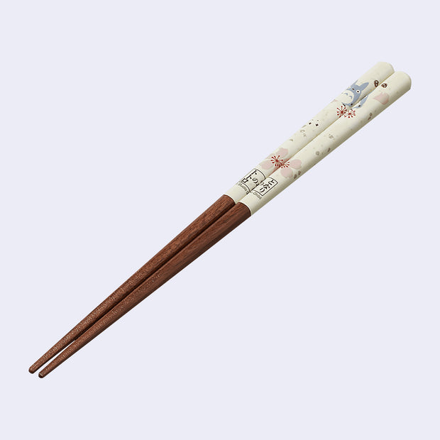Pair of wooden chopsticks with the top half a cream color and illustrations of cherry blossoms and Totoro.