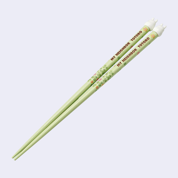 Pair of green chopsticks with small leaf illustrations and "My Neighbor Totoro" written in brown. Small white Totoros top the chopsticks.