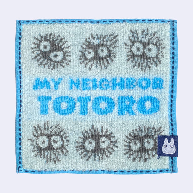 Small square towel, light blue with blue border. Text in center reads "My Neighbor Totoro" in blue and gray soot sprites are around the words.