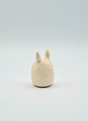Small ceramic figurine with rabbit-like features on a light gray background