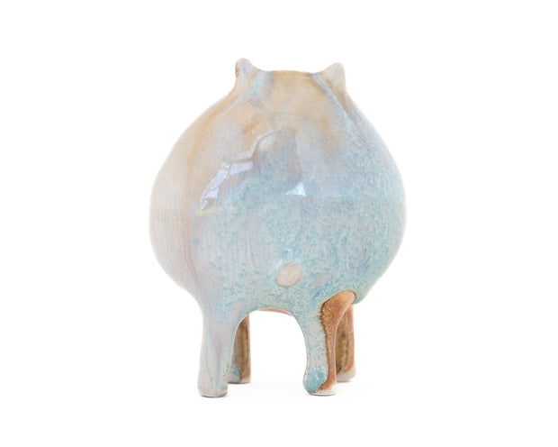 Ceramic sculpture of a character with a rounded body with blue liquid glaze down it. It has small ears and eyes and stands on 4 legs.