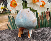 Ceramic sculpture of a character with a rounded body with blue liquid glaze down it. It has small ears and eyes and stands on 4 legs.