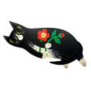 A stylized black cat cut out painting, lying down and holding a red flower with green leaves, shown on a plain white background.