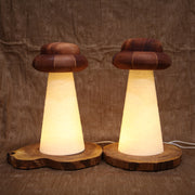 2 wooden lamps, both with UFO shaped tops and conical shaped beams, where light shines through. One lamp has a bean shaped wooden base, the other has a circular wooden base. 
