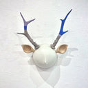 Sculpture of a white round moon-like head with a simple closed eye expression face. It has deer ears and bumpy antlers growing out of its head.