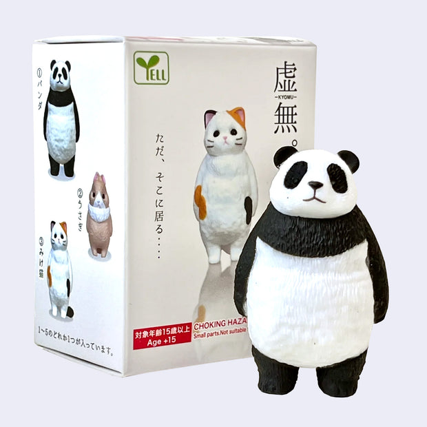 Small figurine of a panda standing on 2 legs and looking straight forward with a blank expression. It stands in front of its product packaging.