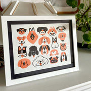 Illustration of 17 dog faces, drawn in orange, black and white. They are done in a very simple, graphic design way. They are of all different breeds and among them is a single dog butt. Framed on a dresser.