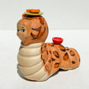 Caterpillar with the face of a Kewpie baby and coloring of a bengal cat. Atop its head is a green plate with an orange fish on it.