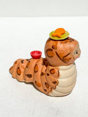 Caterpillar with the face of a Kewpie baby and coloring of a bengal cat. Atop its head is a green plate with an orange fish on it.