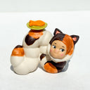 Caterpillar with the face of a Kewpie baby and coloring of a calico cat. Atop its back, is a green plate with an orange fish on it.
