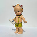 Vintage-style Kepwie doll with green overalls holding a bottle of milk and smoking a cigarette on a white background