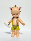 Vintage-style Kepwie doll with green overalls holding a bottle of milk and smoking a cigarette on a white background