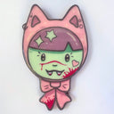 Face of a character with a green face and small, cute fangs. She wears cat ears with a pink bow on a white background