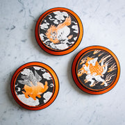 3 black and orange illustrations of yokai on separate black and orange rounded panels.