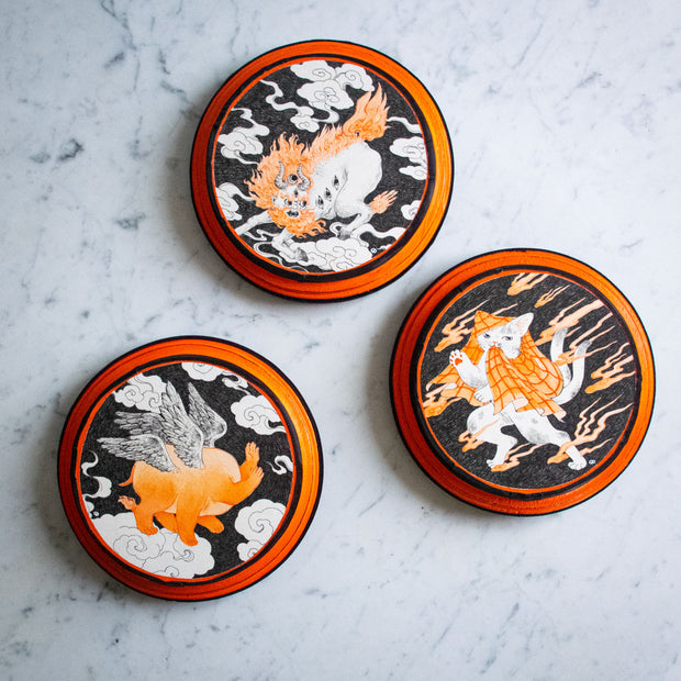 3 black and orange illustrations of yokai on separate round orange and black panels.