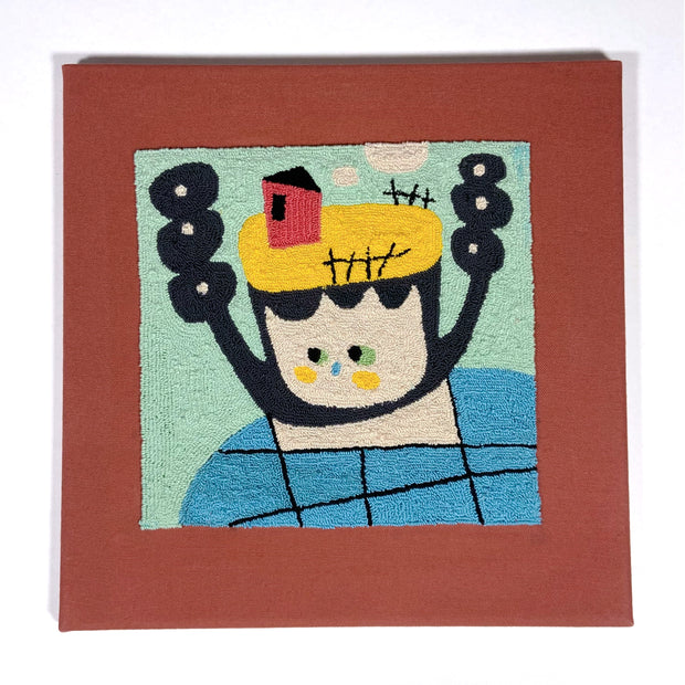 Punch needle illustration of an abstract person with a small house atop its head. Person has round ended black twin tails. On a mint and burnt orange square background.
