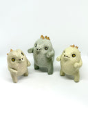Group of 3 ceramic light green baby dinosaur sculptures, with short limbs and gold spikes on their backs. They are made in a stylistically cute way, with rounded eyes and buckteeth. 
