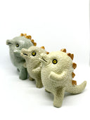 Group of 3 ceramic light green baby dinosaur sculptures, with short limbs and gold spikes on their backs. They are made in a stylistically cute way, with rounded eyes and buckteeth. 