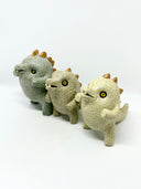 Group of 3 ceramic light green baby dinosaur sculptures, with short limbs and gold spikes on their backs. They are made in a stylistically cute way, with rounded eyes and buckteeth. 