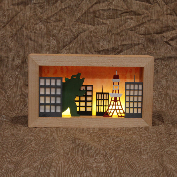 Shadow box depicting Godzilla in “Tokyo” at sunset. Battery operated light will illuminate the background imitating a sunset sky