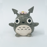 Ceramic figurine of a stylized Totoro with a flower on its head against a white background