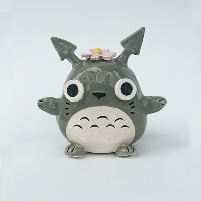 Ceramic figurine of a stylized Totoro with a flower on its head against a white background