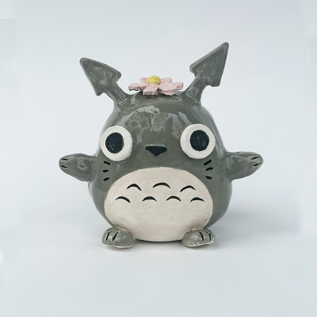 Ceramic figurine of a stylized Totoro with a flower on its head against a white background