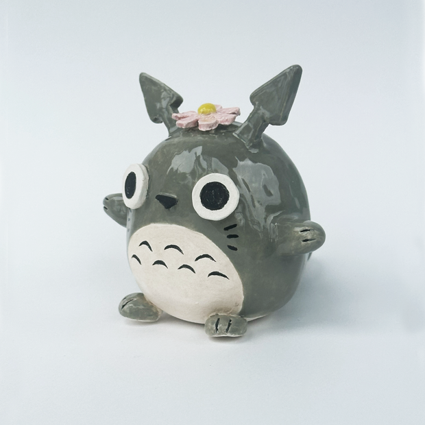 Ceramic figurine of a stylized Totoro with a flower on its head against a white background