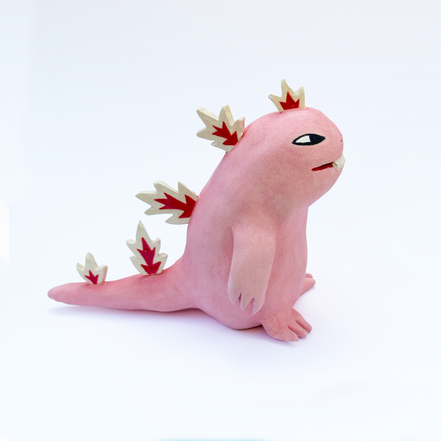 Ceramic sculpture of a chubby, cute cartoonish dinosaur with white and red spikes.