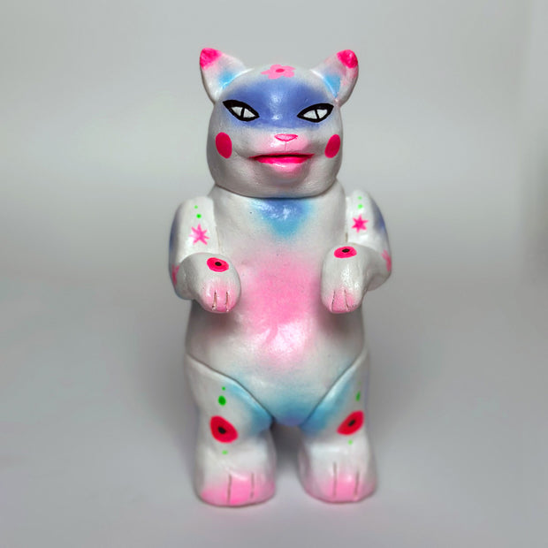 Sculpture made to look like a vinyl Kaiju cat - mostly white in color with spray paint colors of pink, blue and purple.