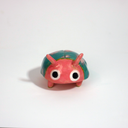 Small ceramic sculpture of a pink bug with large cartoon eyes and a teal blue shell. It has 2 short antenae. 