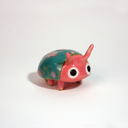 Small ceramic sculpture of a pink bug with large cartoon eyes and a teal blue shell. It has 2 short antenae. 