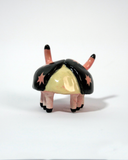 Small ceramic sculpture of a pink and black bug with a cute cartoon face.