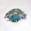 Ceramic sculpture of a cartoon beetle, with a teal head and large cartoon style eyes. Its body is a grayish green with dots.