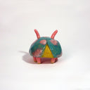 Small ceramic sculpture of a pink bug with large cartoon eyes and a teal blue shell. It has 2 short antenae. 