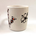White ceramic cup with black floral designs on a white background