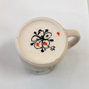 Ceramic mug with a decorative design on the bottom to accompany the artist signature on a white background