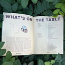 Open magazine with text that reads "what's on the table" with a table of contents and illustrations on a green leafy background
