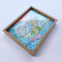 Framed artwork of a seal taking a bath in a bathtub with a spread of sea food in front of it. Water flows out of the tub.