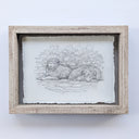 A monochrome pencil-style artwork showing two fluffy dogs resting in front of leafy branches, centered on a white background with a lightly textured border around the drawing.
